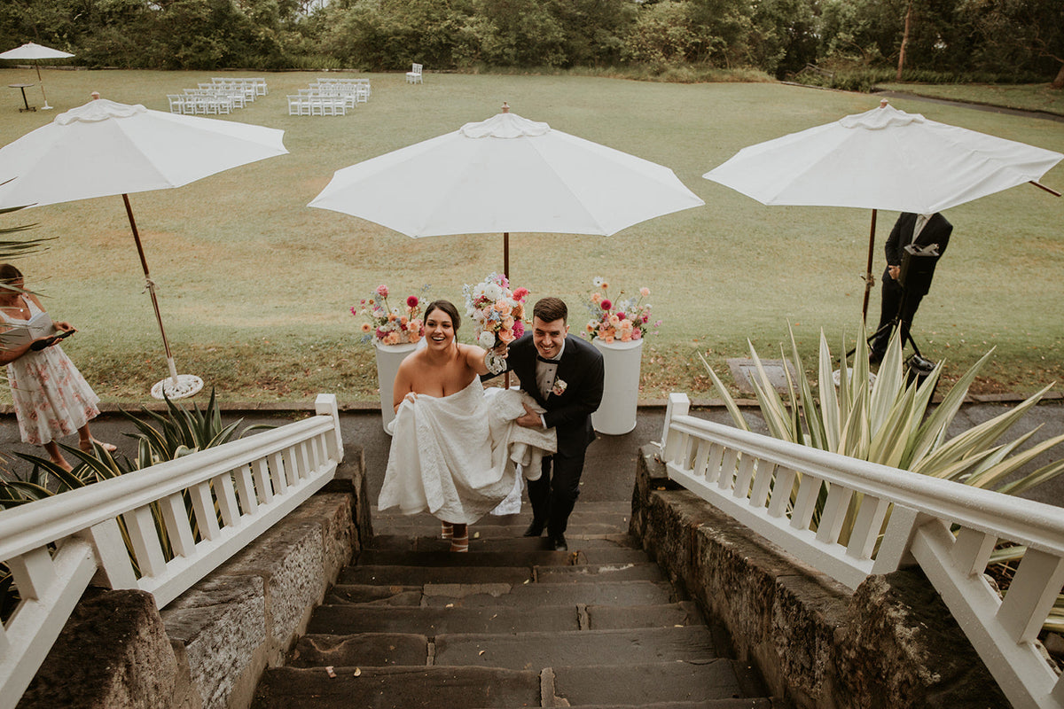 Couple walking up the stairs from the Athol Hall lawn past plinth arrangements and white market umbrellas