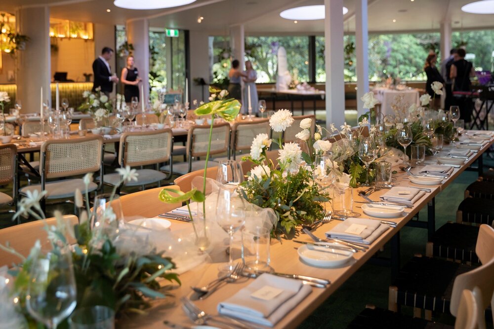 Long tables with white and green flowers and anthuriums in the glass-walled room at Terrace on the Domain