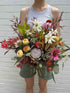 A fresh bouquet of Christmas flowers featuring a variety of colorful flowers such as red, white, and pink, held by a person against a brick wall background.