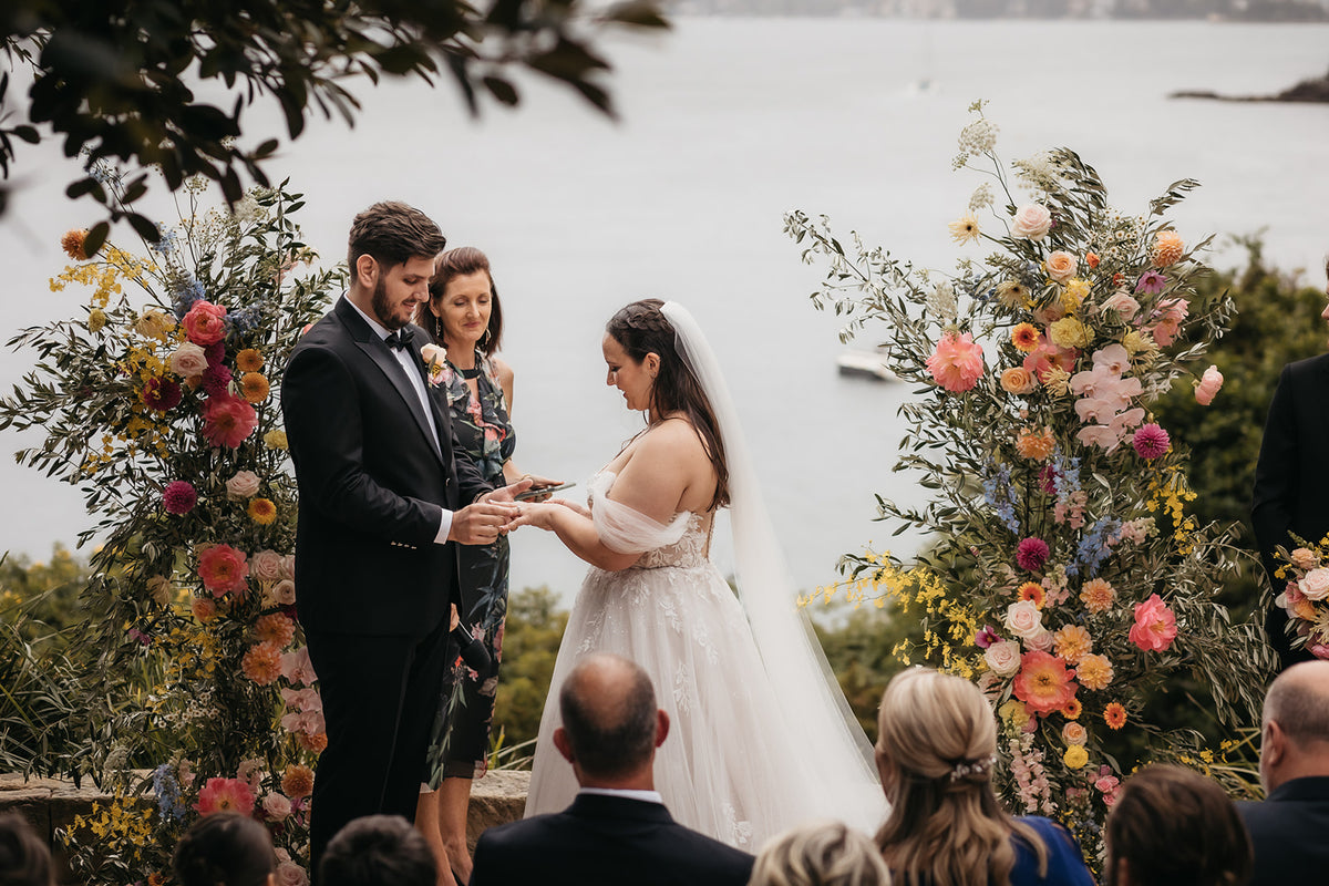 Couple exchanging vows between two colourful floral installations at Sergeants Mess
